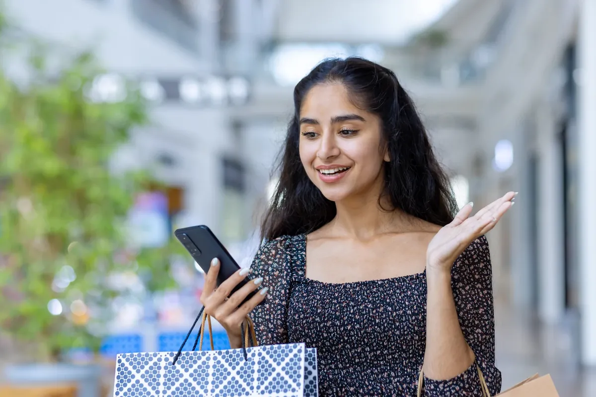 Smiling woman looking at her phone while holding shopping bags