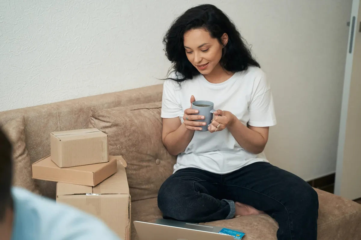 A woman on a sofa holding a mug, with delivery parcels beside her