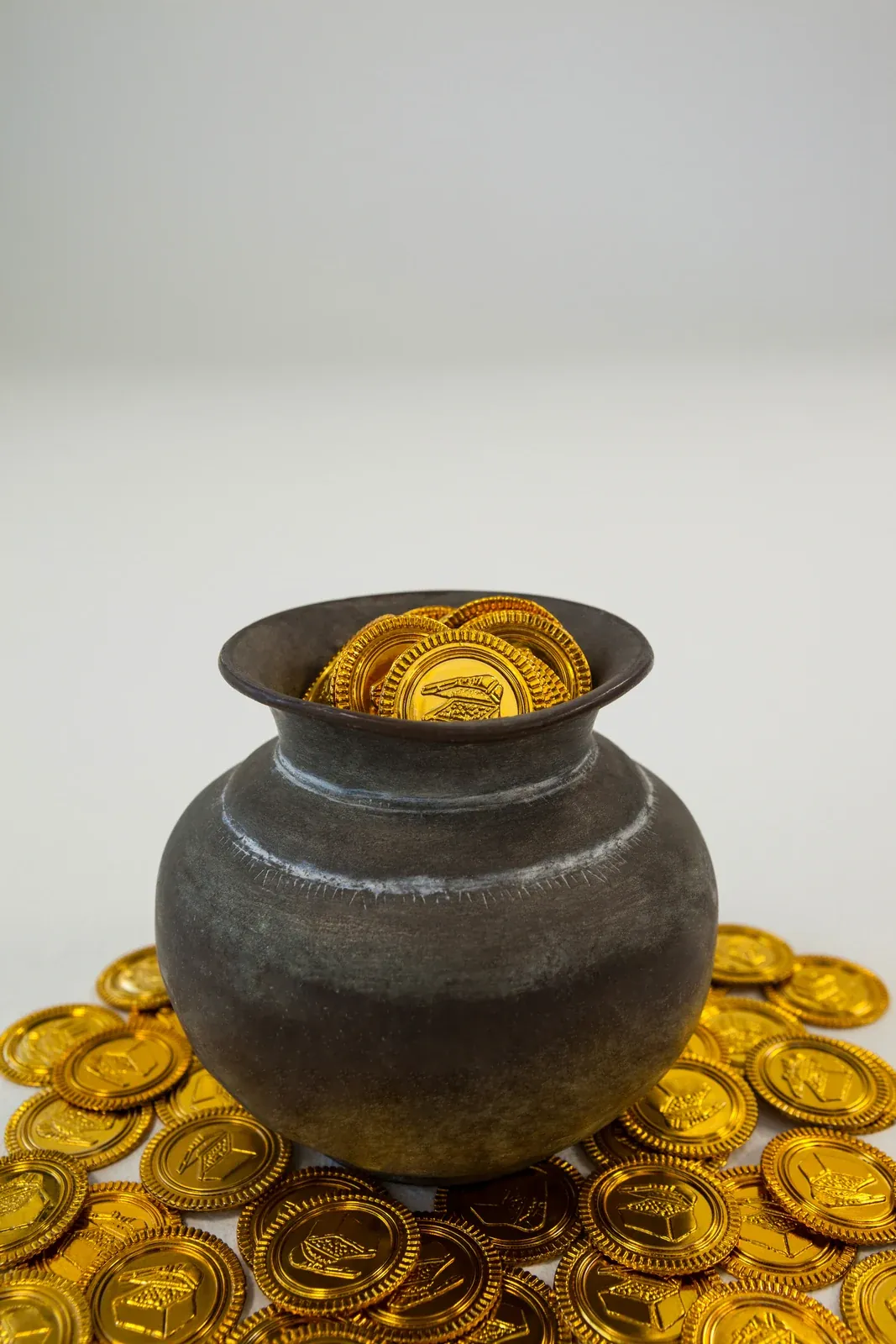 A clay pot overflowing with gold-coloured coins, with more coins on the surface around it