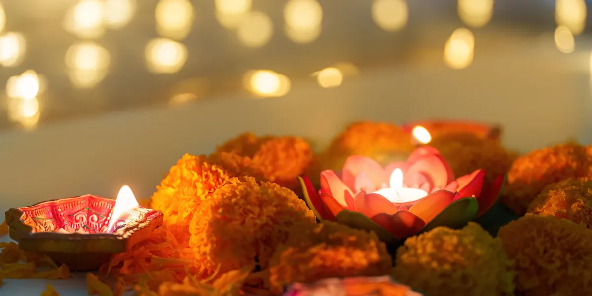 A lit clay diya and a lotus-shaped tealight surrounded by orange marigold flowers, with soft golden lights blurred in the background