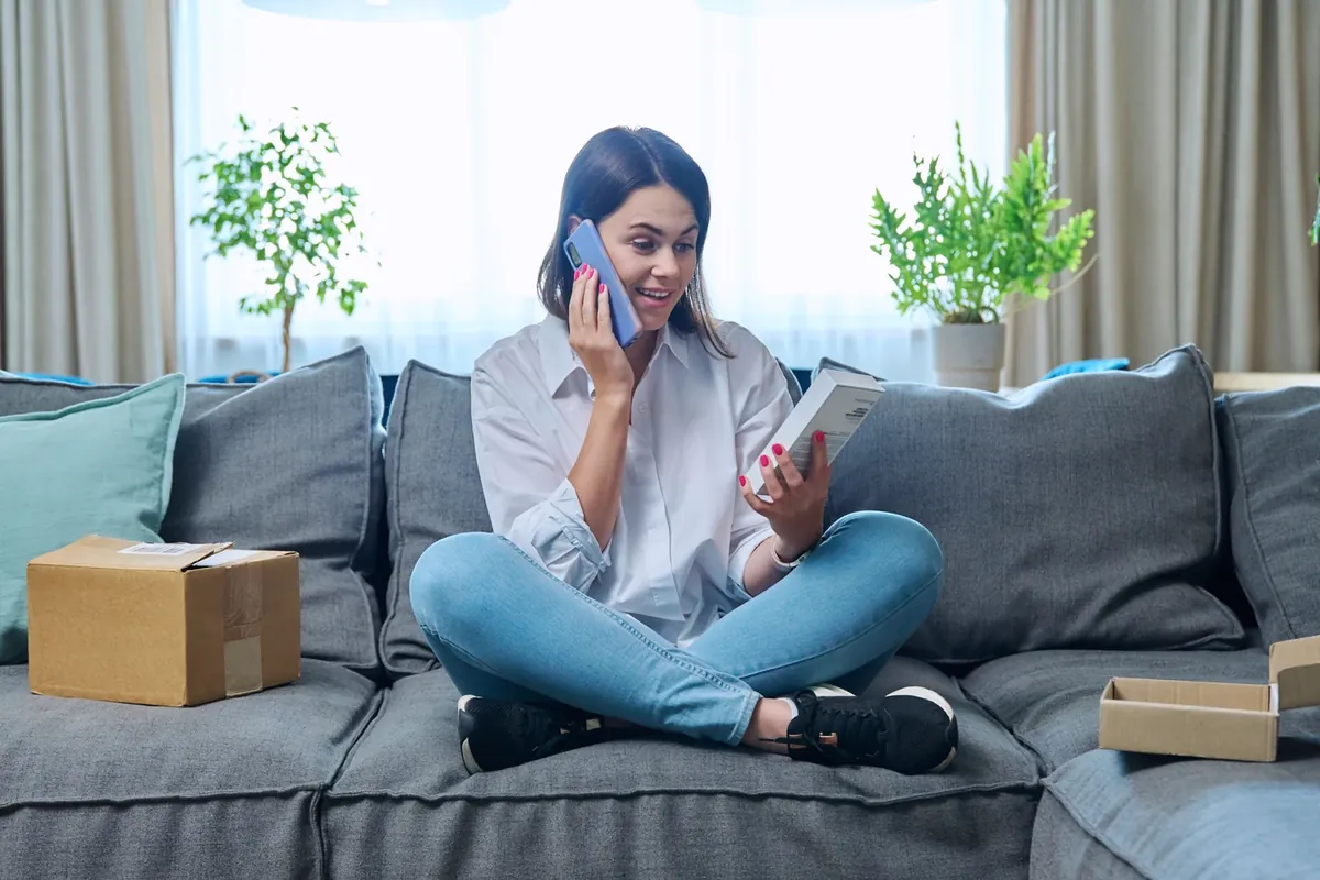 Woman on a phone call holding a delivery package on a sofa