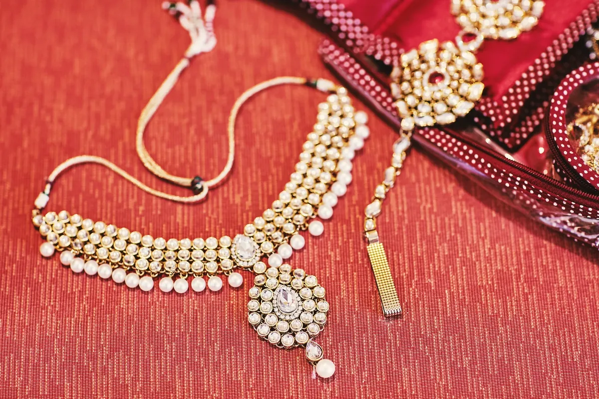 A gold-toned choker necklace with pearl drops and a matching ornament laid on red fabric