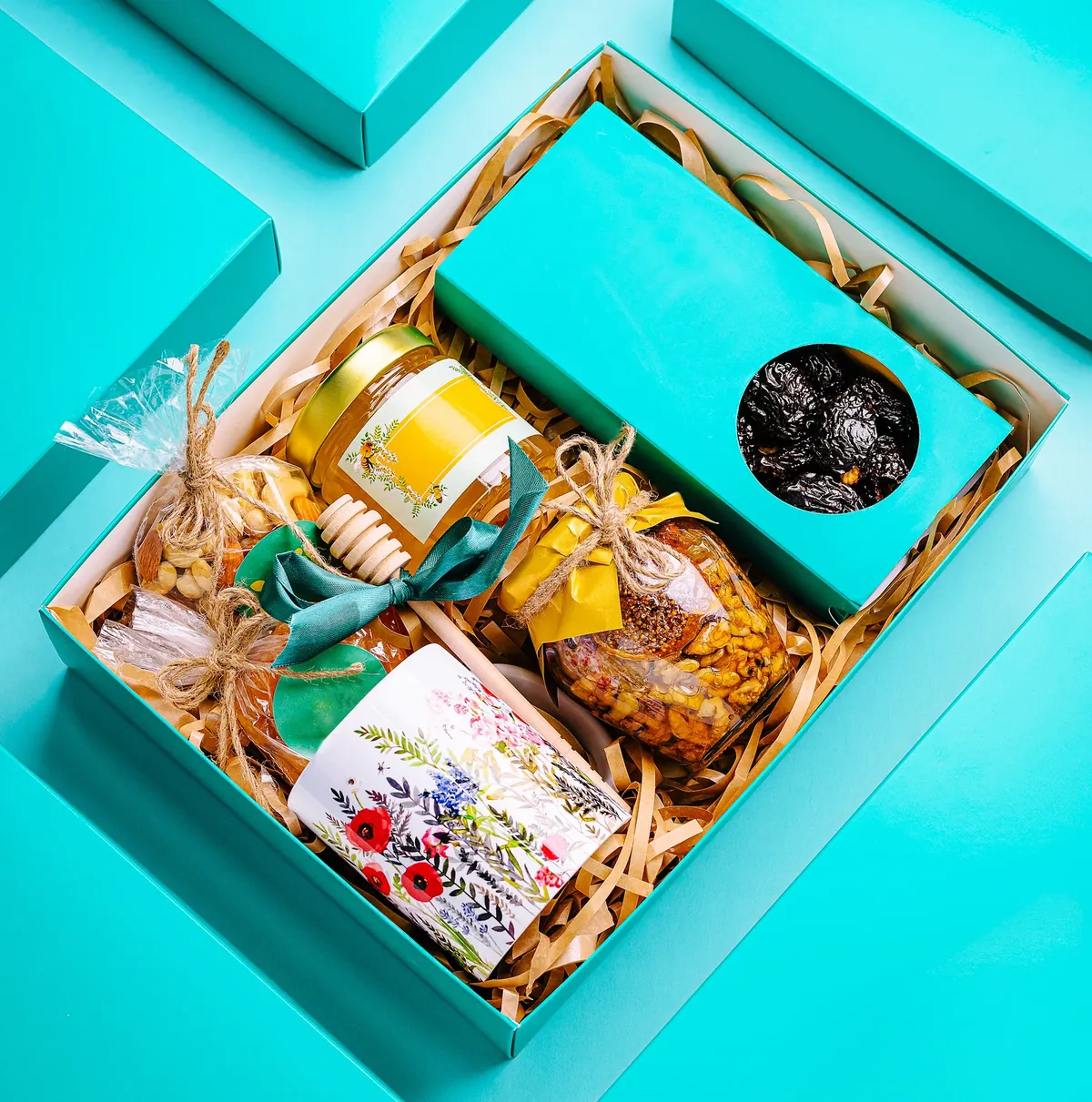 Open teal gift hamper packed with a honey jar, mixed nuts, dried fruit and a floral-labelled jar