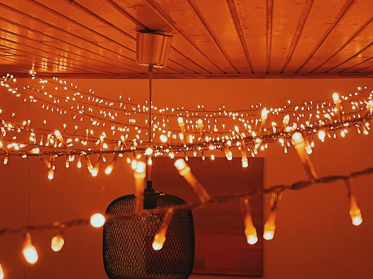 Warm-white string lights draped in loops across a wooden ceiling beside a black mesh pendant lamp, glowing orange