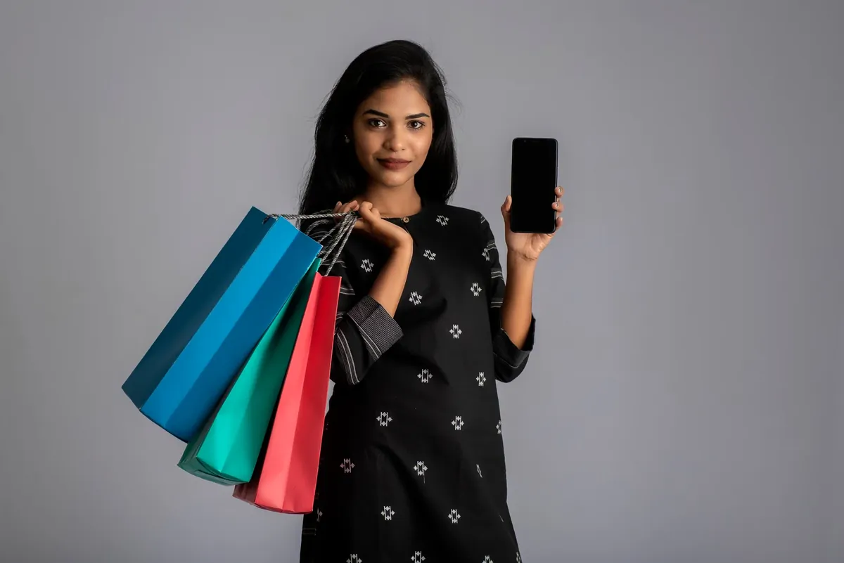 A woman in a black printed kurta holding a phone and several colourful shopping bags
