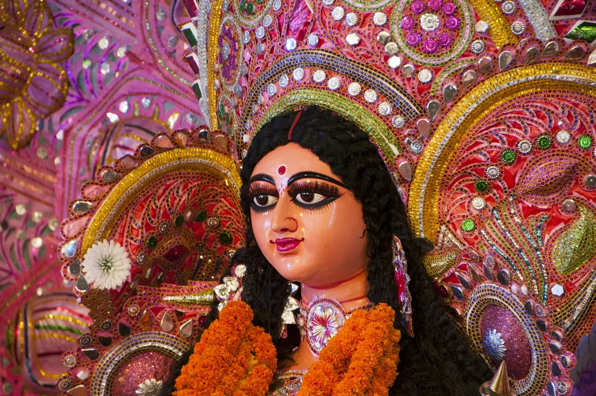 Close-up of a decorated Durga idol with a jewelled crown and an orange marigold garland