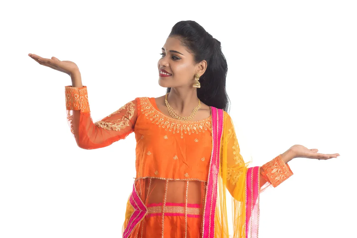 Woman in an orange chaniya choli with a dupatta dancing with her arms outstretched