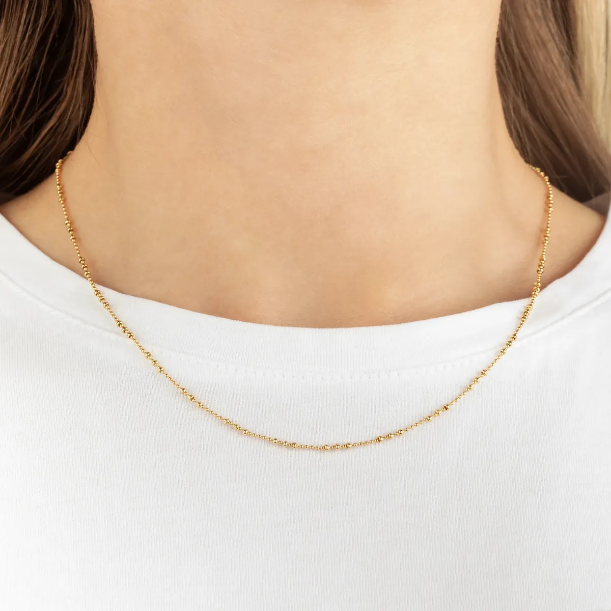 A thin gold chain worn with a plain white t-shirt, close-up of the neckline