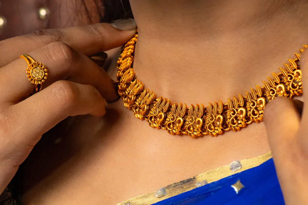 A close-up of an antique-finish gold necklace and ring on a woman wearing a blue saree