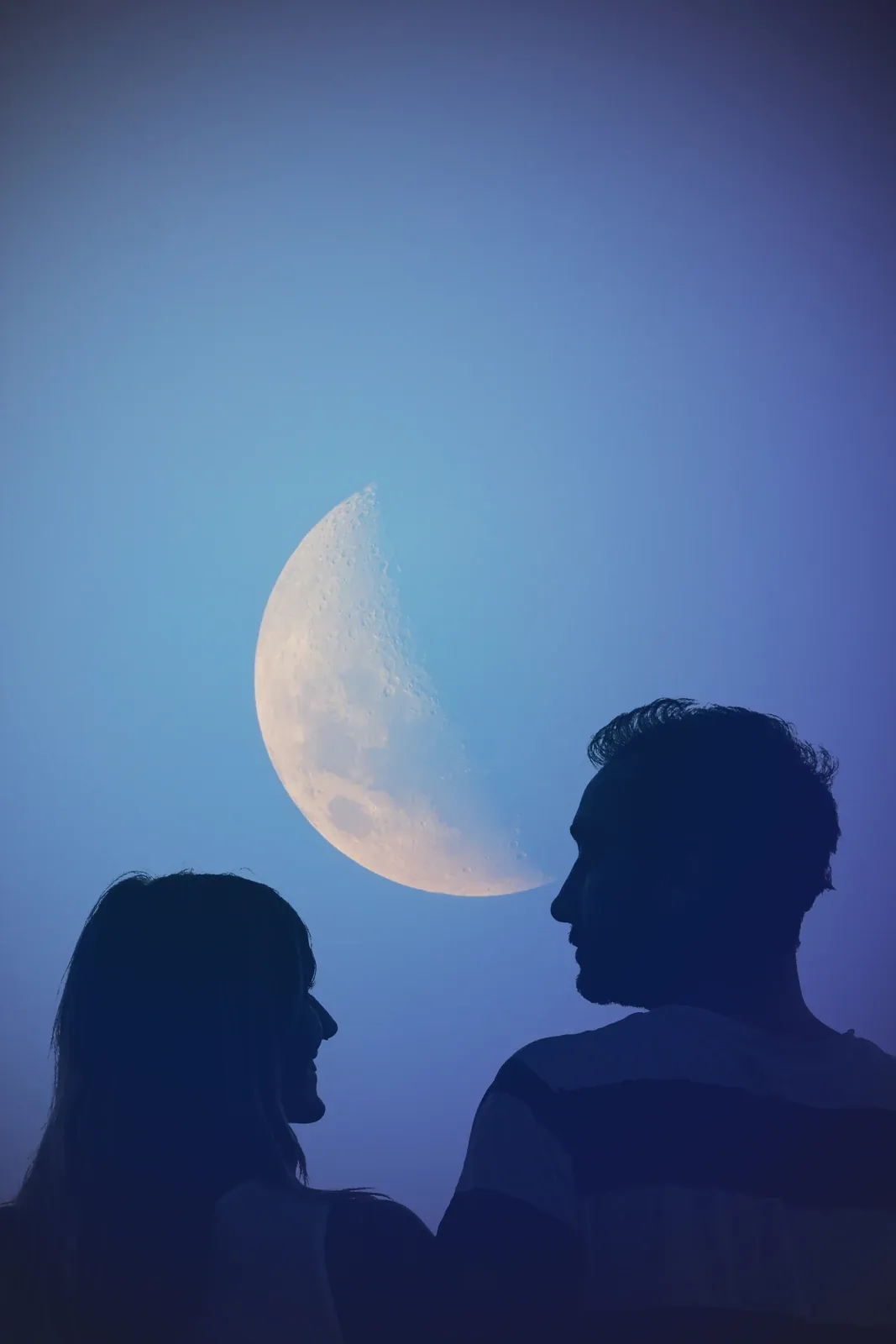 Silhouettes of a woman and a man facing each other against a blue evening sky with a half moon between them