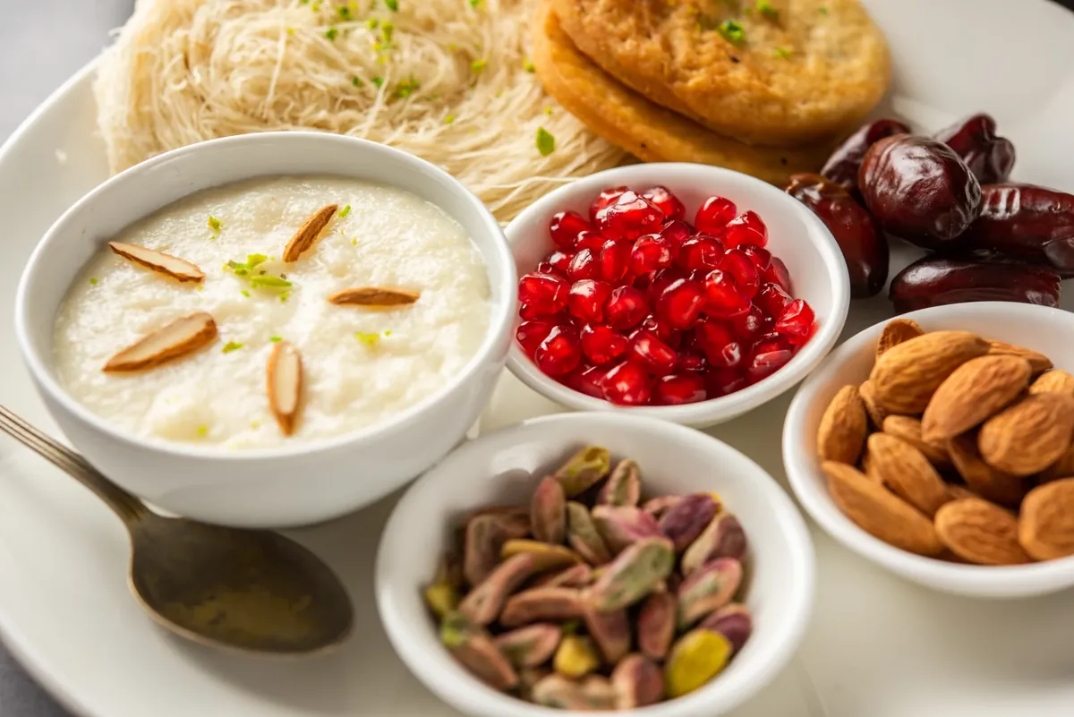 A plate with a bowl of kheer topped with almonds, pomegranate seeds, dates, pistachios and almonds