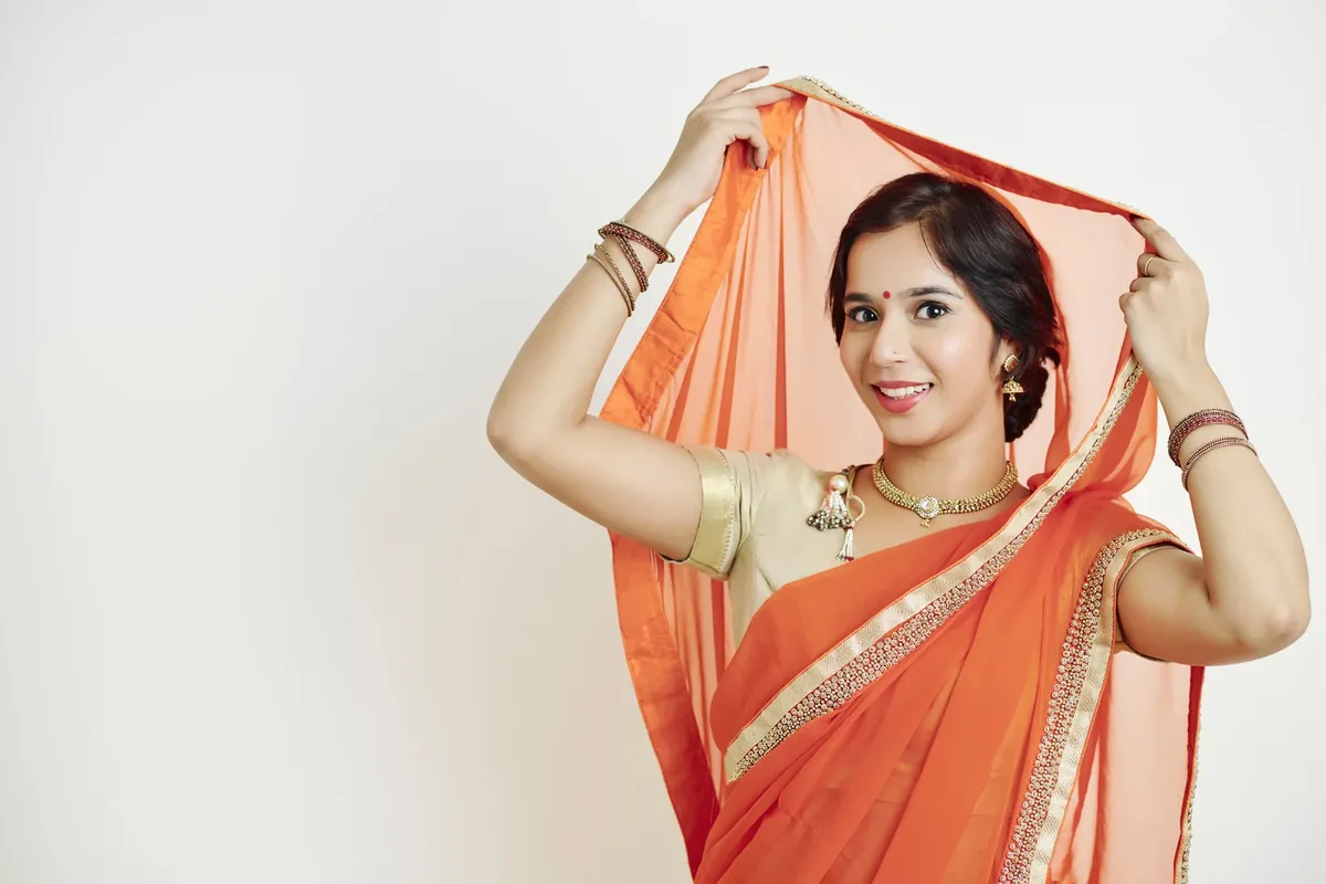 A woman wearing a sheer orange dupatta draped over her head and shoulder