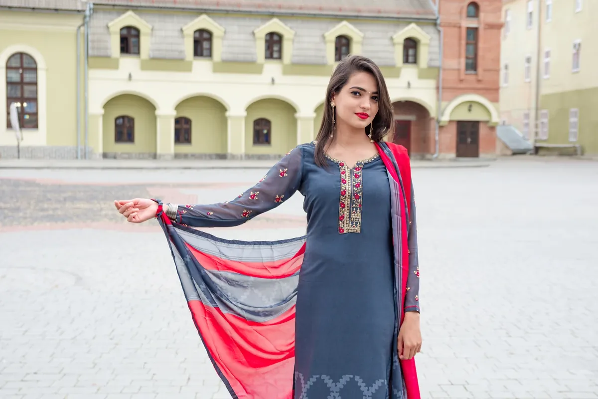 A woman in a grey embroidered kurta set holding out a pink and grey dupatta