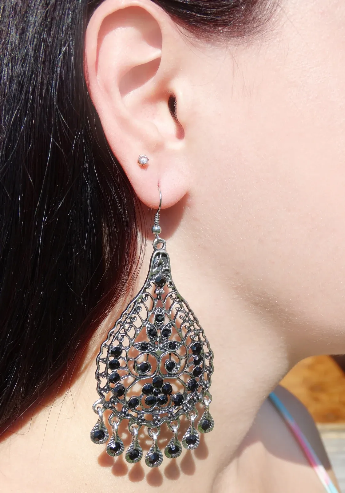 Close-up of a large oxidised silver teardrop earring with black stones worn on an ear