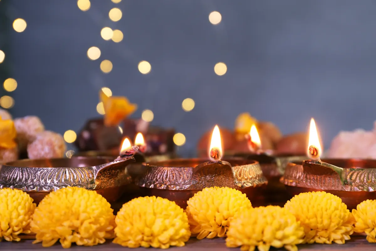 Lit brass oil lamps with decorated rims in a row, with yellow chrysanthemum flowers in front and soft round lights behind